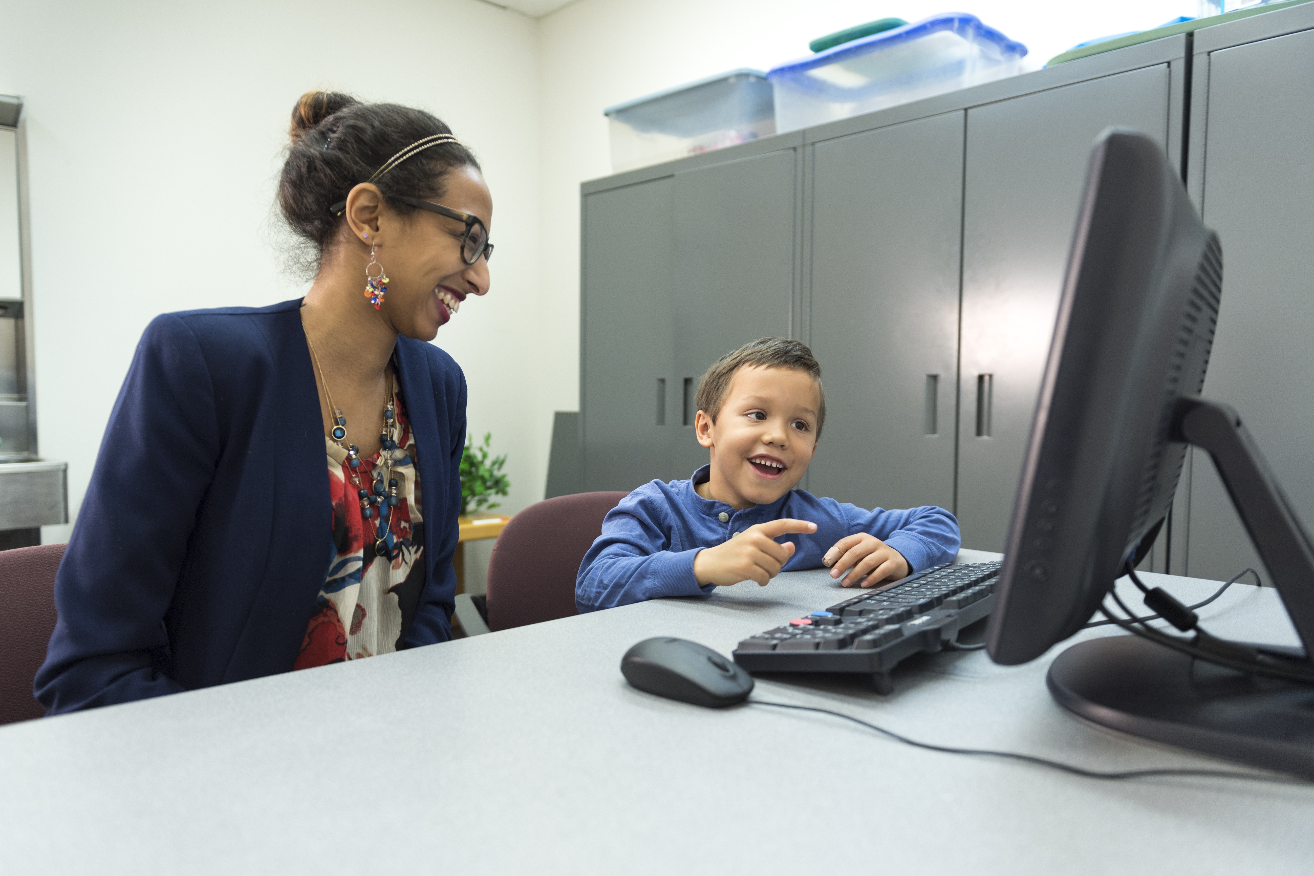 Researcher assisting a young boy with a computer task.